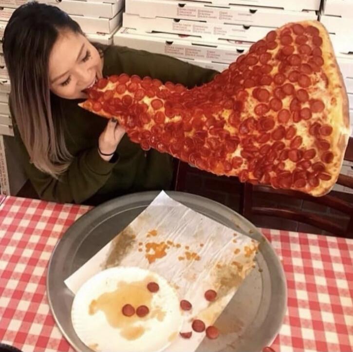 A person eating a giant slice of pepperoni pizza at a table.