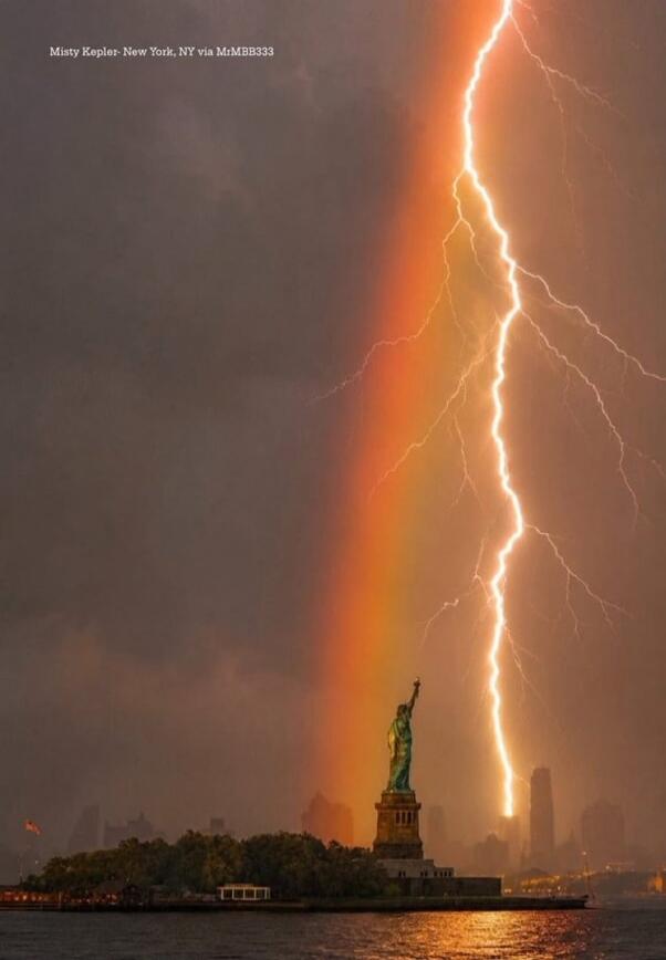 Misty Kepler - New York, NY via MrMBB333. A dramatic photograph captures a lightning bolt striking near the Statue of Liberty in New York City, with a vibrant rainbow visible in the stormy sky.