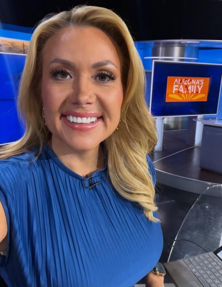 A woman in a blue pleated top smiles at the camera in what appears to be a news studio. In the background, a screen displays 'ARIZONA'S FAMILY'.