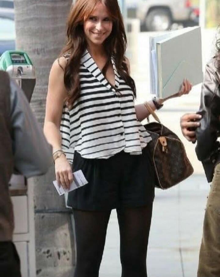 A smiling Jennifer Love Hewitt walking outdoors, holding documents, a handbag, and some papers.