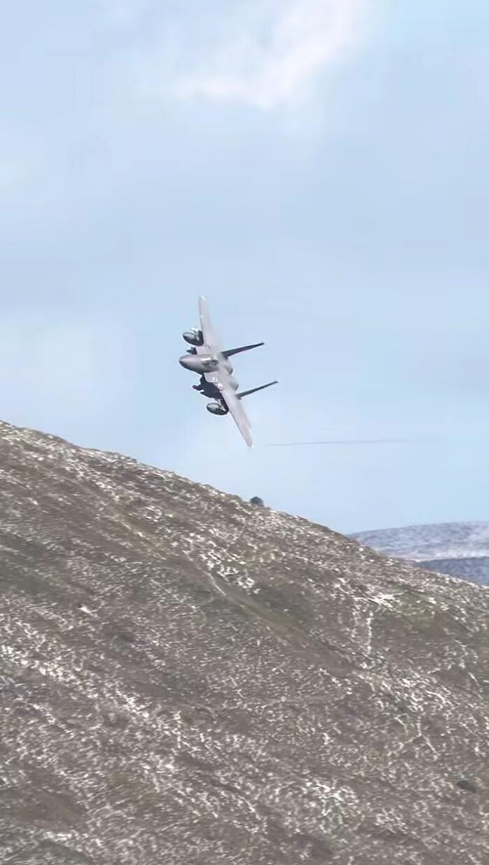 An aircraft flying low over a mountainous landscape, performing a steep bank or roll.