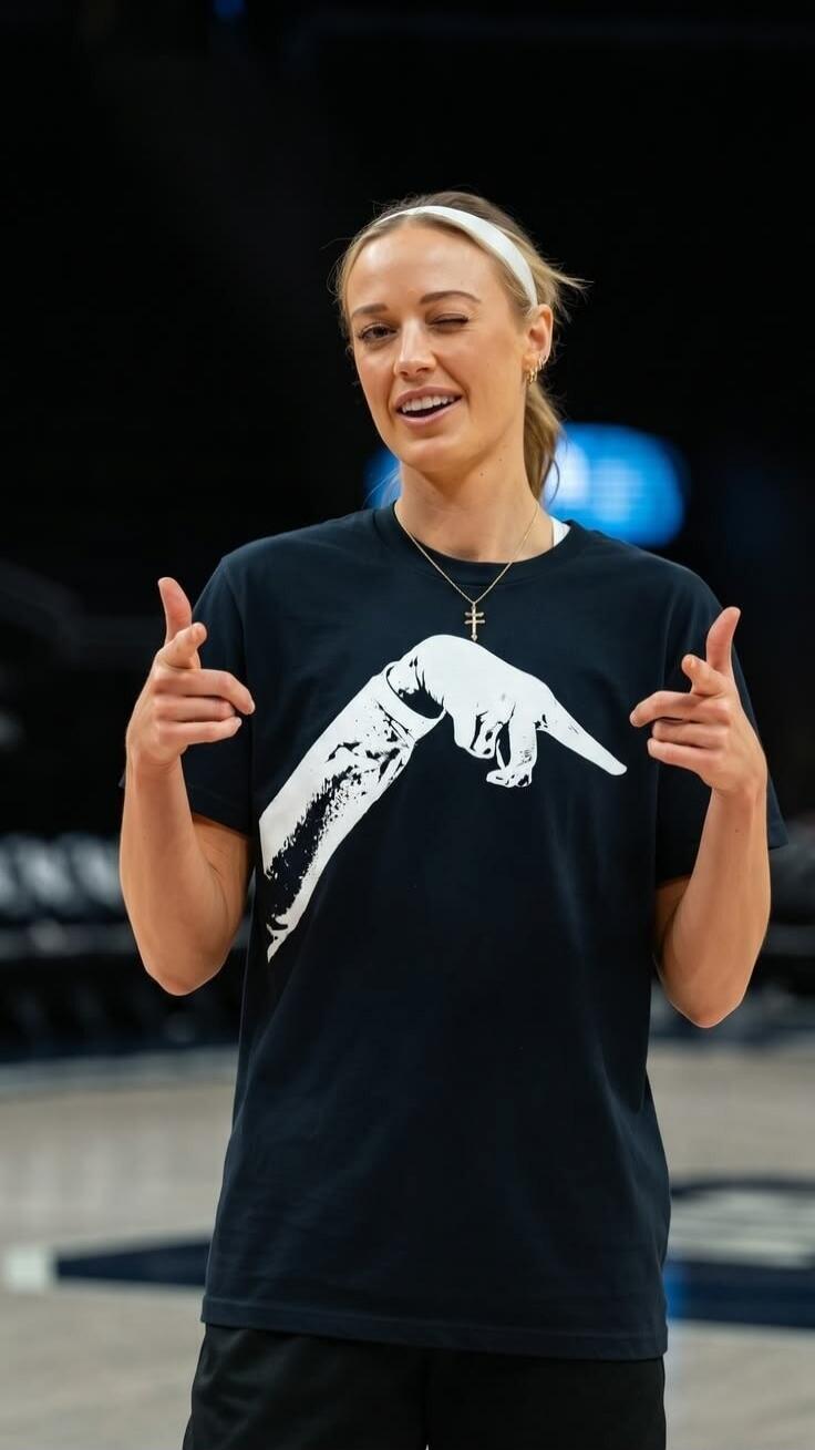 A woman winking and making finger gun gestures with both hands. Her t-shirt features a graphic of two hands pointing.