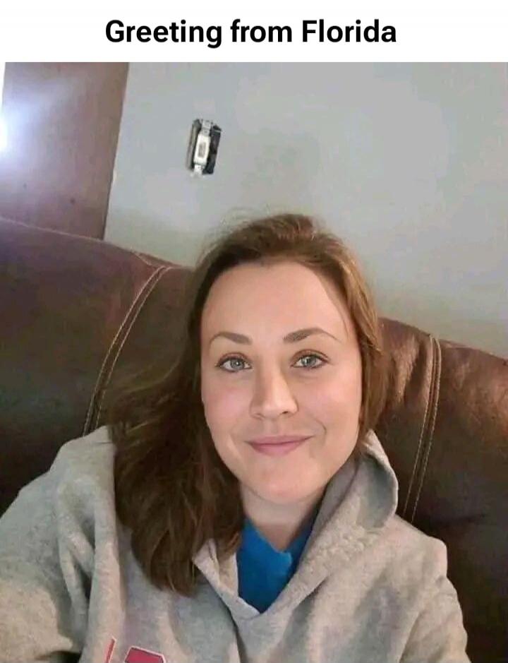A woman takes a selfie, smiling at the camera. Above her head, an electrical outlet is visibly hanging out of the wall. The text overlay reads: 'Greeting from Florida'. The image implies a humorous take on the 'Florida Man' stereotype or general chaos associated with the state.