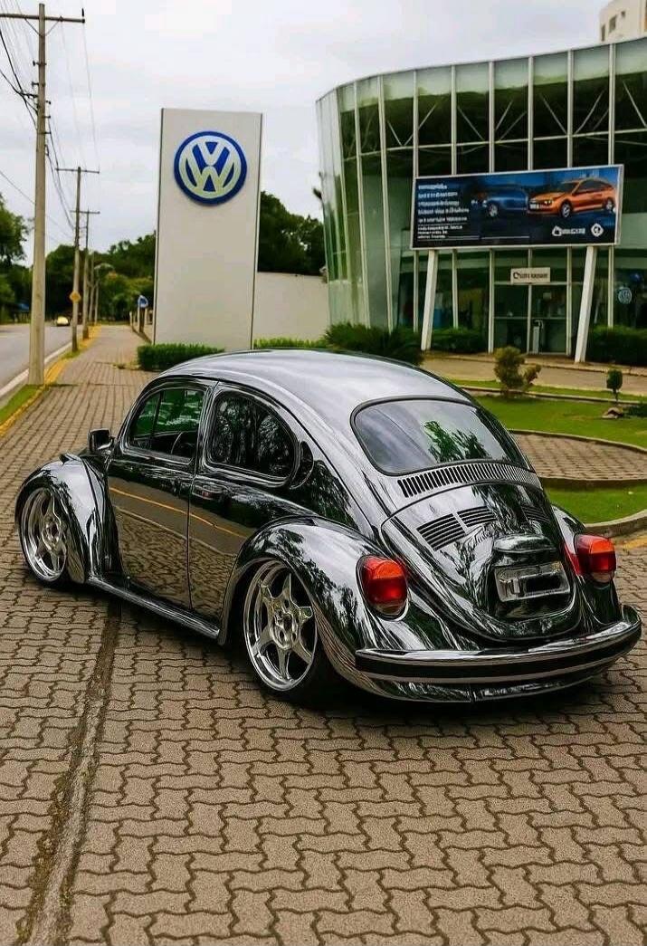 A chrome-plated Volkswagen Beetle parked outside a Volkswagen dealership.