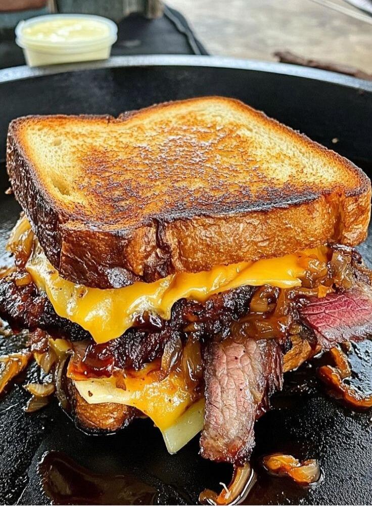 A grilled beef melt sandwich with caramelized onions and melted cheese on toasted bread.