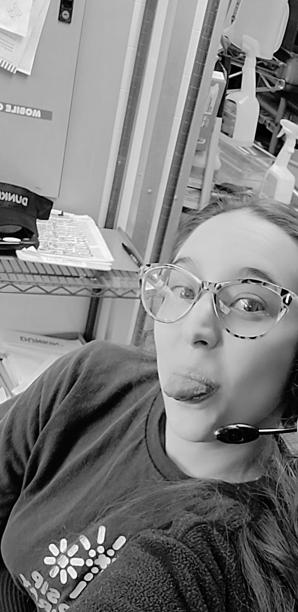 A person wearing glasses and a headset, sticking their tongue out, with a 'Dunkin'' cap visible in the background. Other text visible includes 'WOBITE C'.