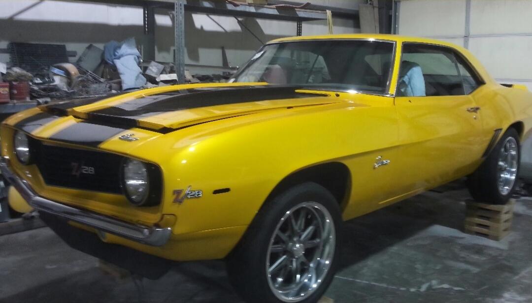Yellow vintage muscle car (likely a Chevrolet Camaro Z/28) with black racing stripes and raised hood.