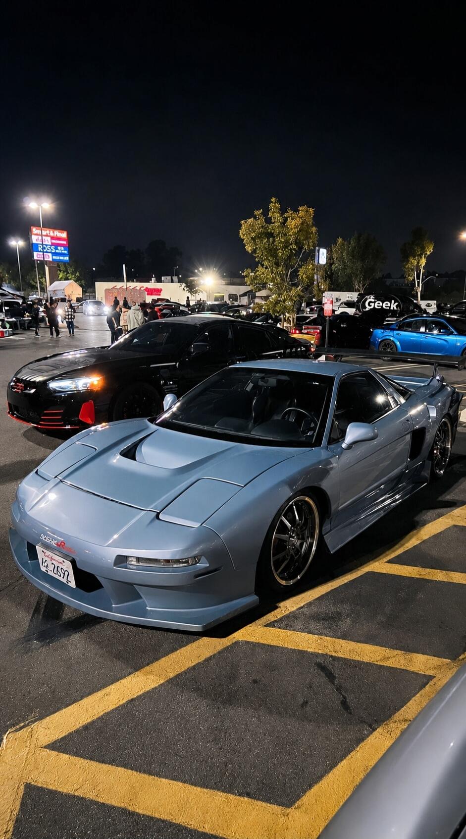 Smart & Final, ROSS, California 4Z 2692, NSX-R, Geek. A night car meet in a parking lot featuring a light blue Acura NSX and a black Kia Stinger, with other cars and people in the background.