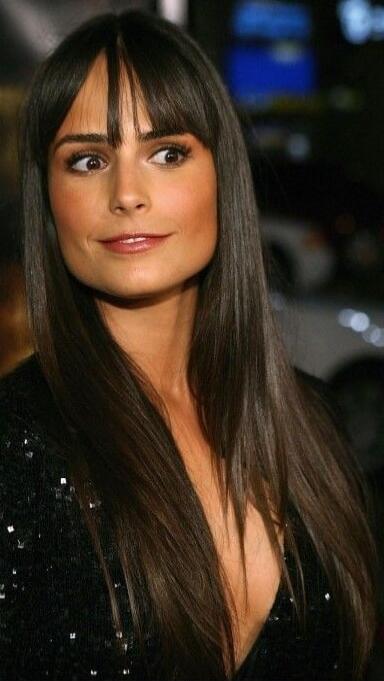 Woman with long dark hair and bangs wearing a black sequin dress, looking to the side.