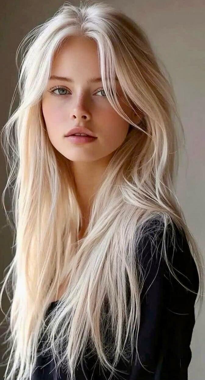 A portrait of a young woman with long platinum blonde hair, wearing a black top.