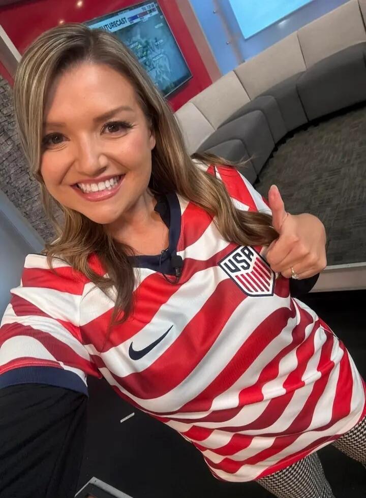 A smiling woman in a USA soccer jersey gives a thumbs-up in a TV studio. The screen in the background shows 'FUTURECAST'.
