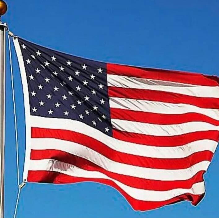 United States flag waving in the wind against a clear blue sky.
