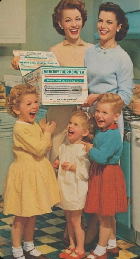 Two women and three children are laughing joyfully in a kitchen. The women are holding product boxes. One box is clearly labeled 