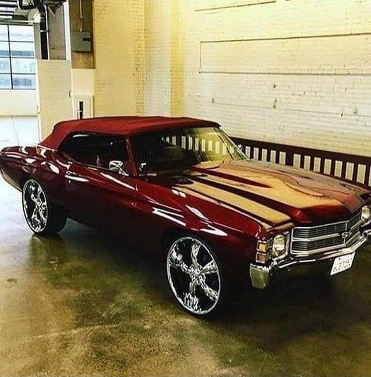 A classic red convertible car with chrome rims is parked indoors.