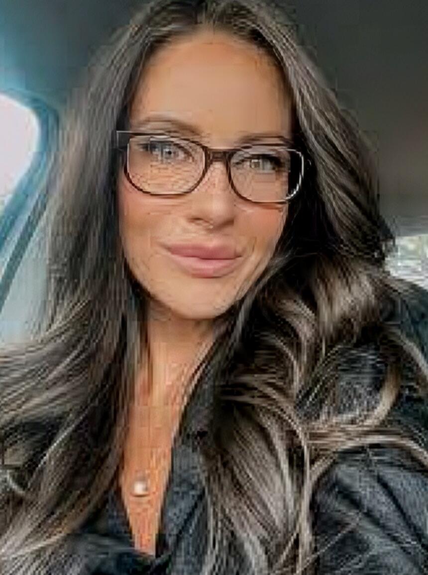 A woman wearing glasses in a car, smiling.