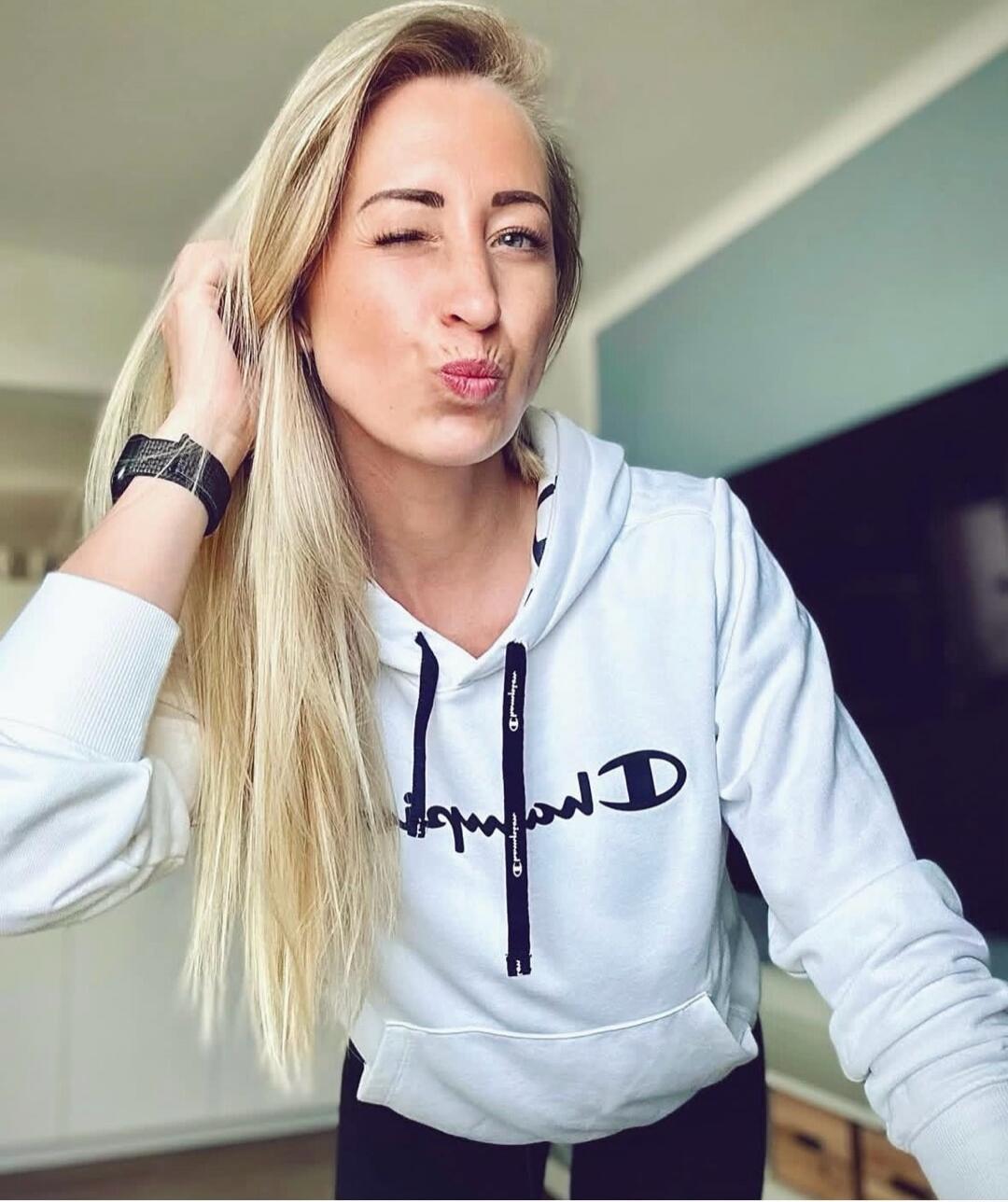 Selfie of a blonde woman wearing a white Champion hoodie, winking at the camera.