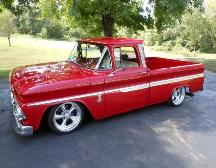 A red vintage pickup truck parked on a driveway under trees.