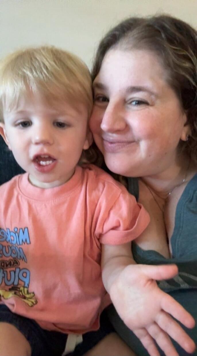 A woman and a young child are smiling together. The child is wearing a t-shirt with a graphic that appears to be Mickey Mouse and Pluto.
