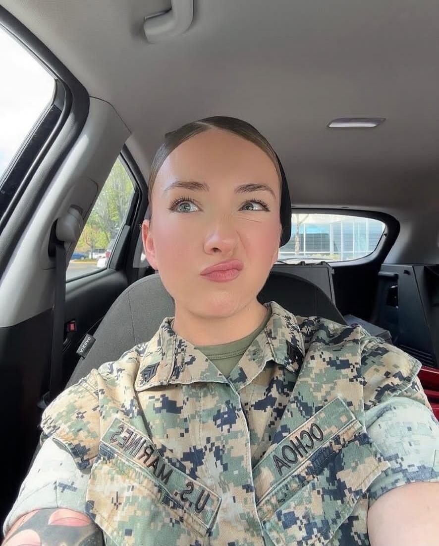 Selfie of a woman in camouflage military uniform making a puckered lips face inside a car.