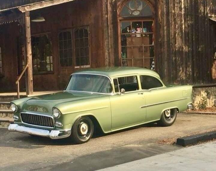 Vintage light-green classic car parked in front of a weathered wooden building.