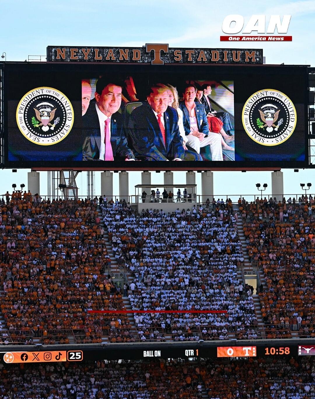 NEYLAND STADIUM. OAN One America News. SEAL OF THE PRESIDENT OF THE UNITED STATES. Donald Trump and other individuals are shown on the large screen. Below, a scoreboard displays 'BALL ON', 'QTR 1', 'O T 10:58', and '25' alongside social media icons.