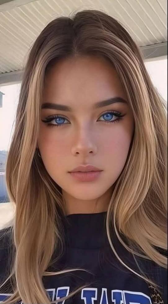 Portrait of a young woman with blue eyes and blonde hair, wearing a dark top.