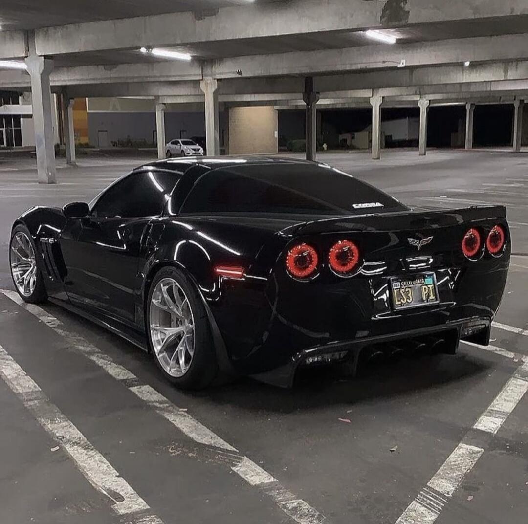 Black Corvette sports car parked in an empty multi-story garage.