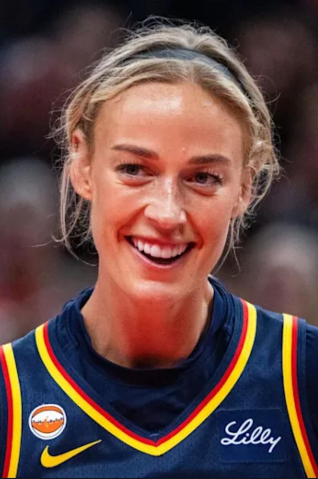 A smiling blonde woman in a basketball jersey. Text on jersey: Lilly. Logos: Nike swoosh, basketball logo.