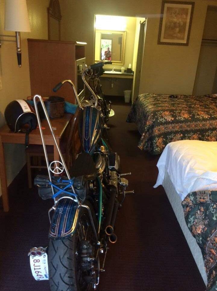 A motorcycle is parked inside a hotel room, between two beds.