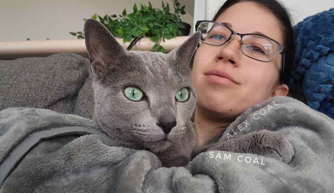 A woman cuddling a gray cat wrapped in a blanket.
