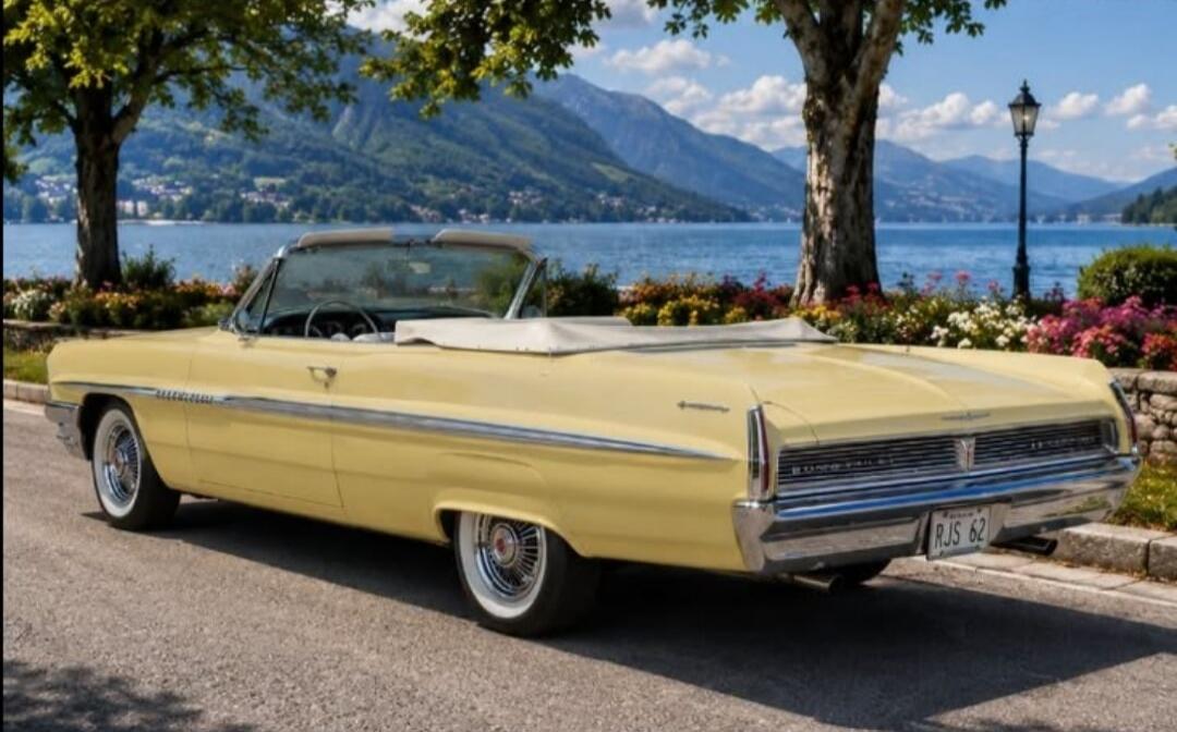 A vintage yellow convertible car is parked by a scenic lake with mountains in the background.