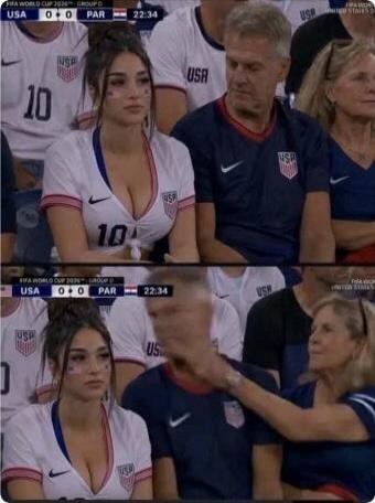 FIFA WORLD CUP 2026 - GROUP G USA 0+0 PAR 22:34. A young woman in a USA soccer jersey with a deep V-neck is sitting at a match. An older woman reaches over a man to touch the young woman's face or shoulder, seemingly in disapproval.