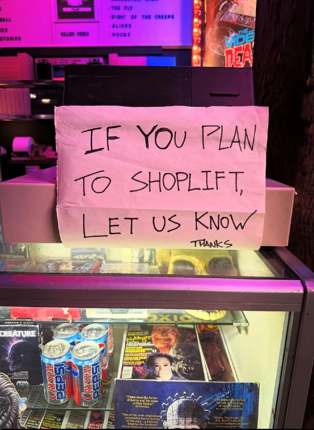 IF YOU PLAN TO SHOPLIFT, LET US KNOW THANKS. Also visible are various horror movie titles and magazines, and Crystal Pepsi cans.