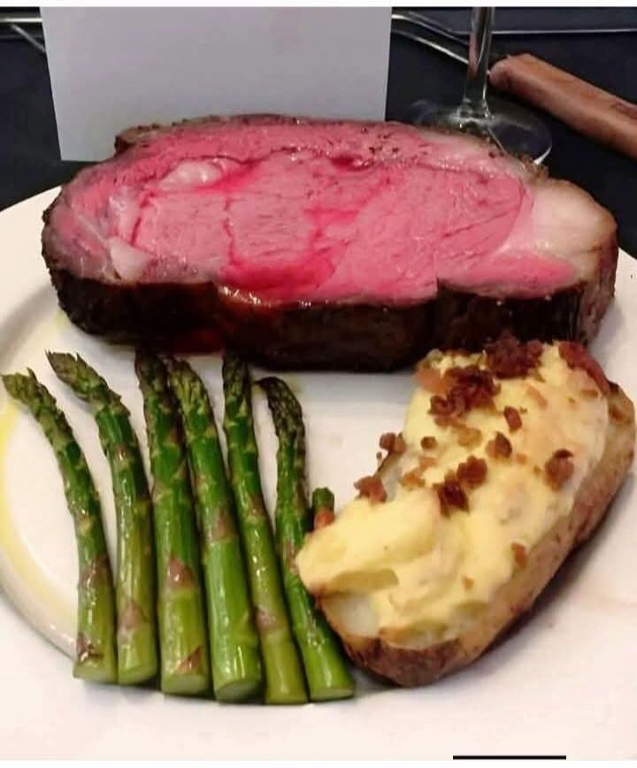 Thick slice of rare steak with asparagus spears and a potato-topped bread slice on a plate.