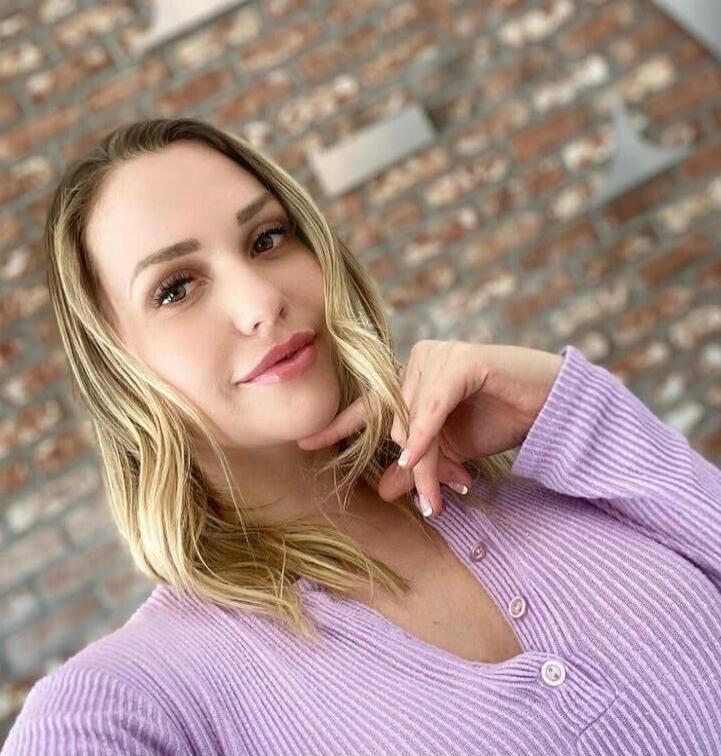 A woman wearing a lavender knit sweater posing in front of a brick wall.
