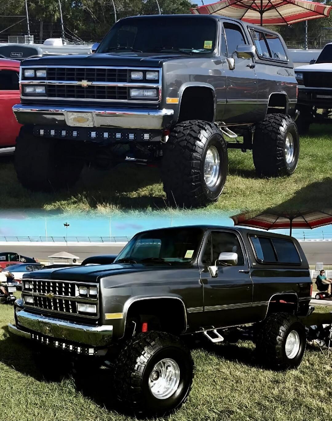 Two heavily lifted Chevrolet trucks with oversized off-road tires on a grassy display at a car show. The front grilles feature Chevrolet bowties.