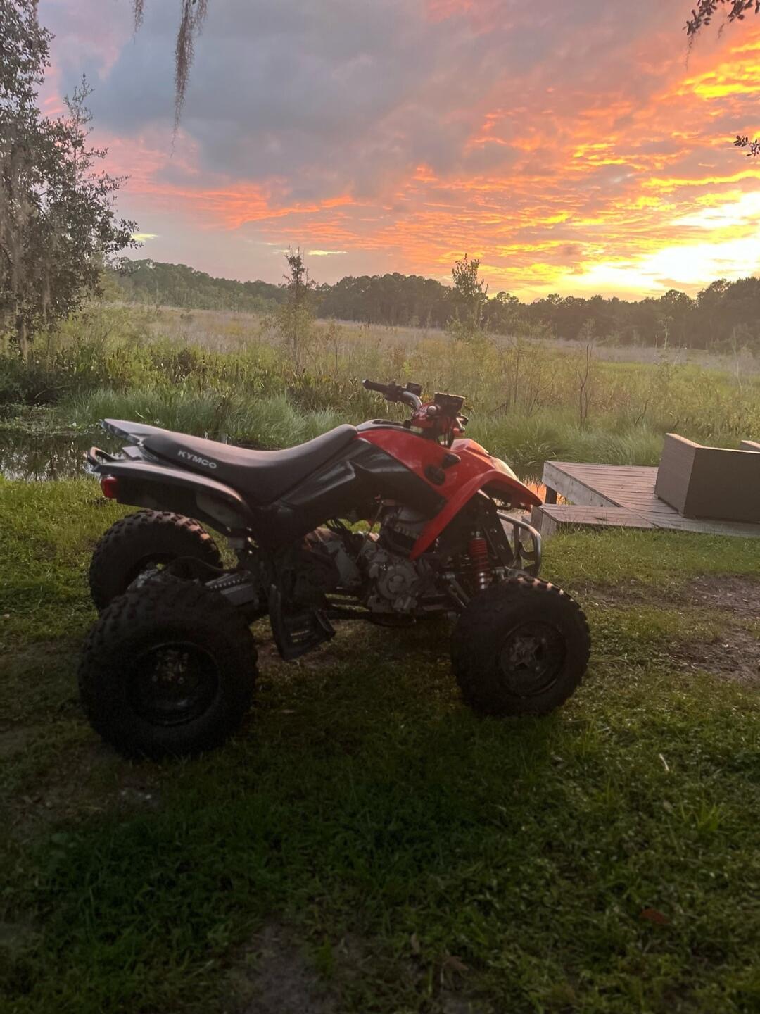 KYMCO. An ATV parked on grass with a beautiful sunset in the background.