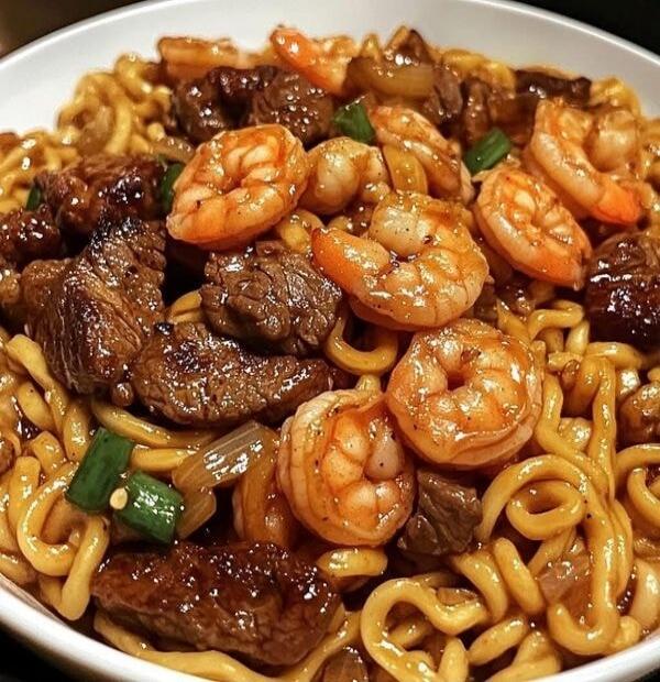 Beef and shrimp noodle dish with sliced beef, shrimp, onions and green onions over fried noodles.