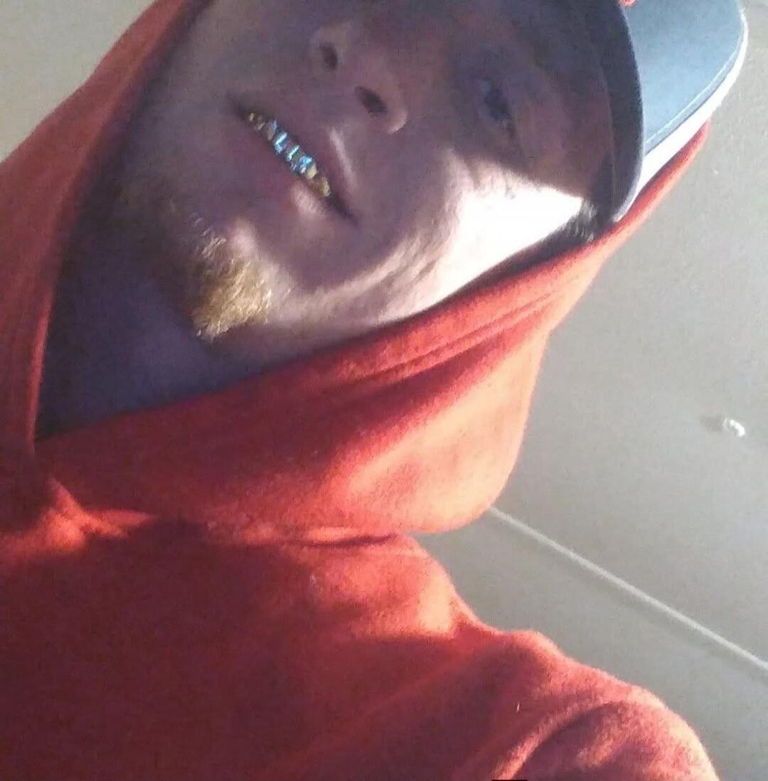 A person wearing a red hoodie and a cap, showing off grillz on their teeth.