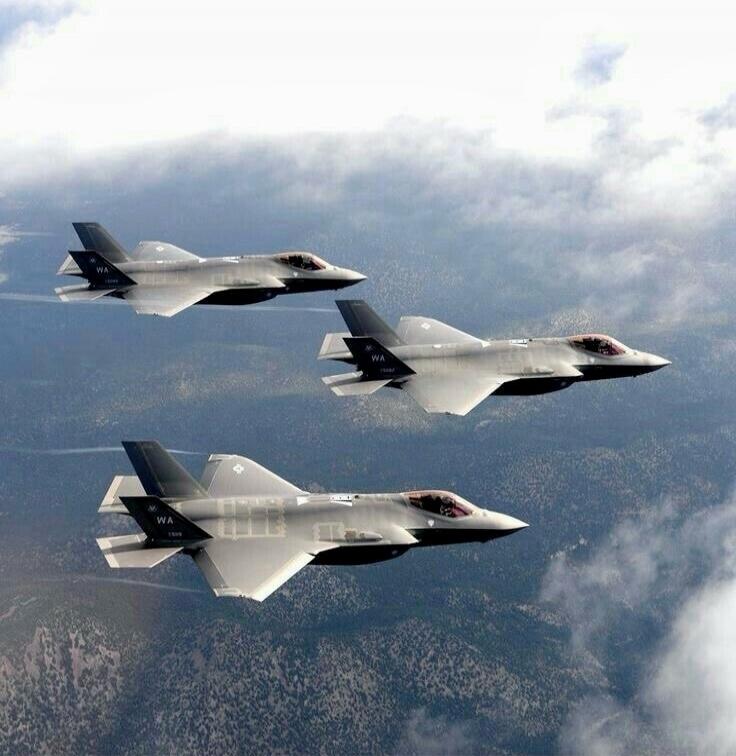Three stealth fighter jets flying in formation above a landscape.