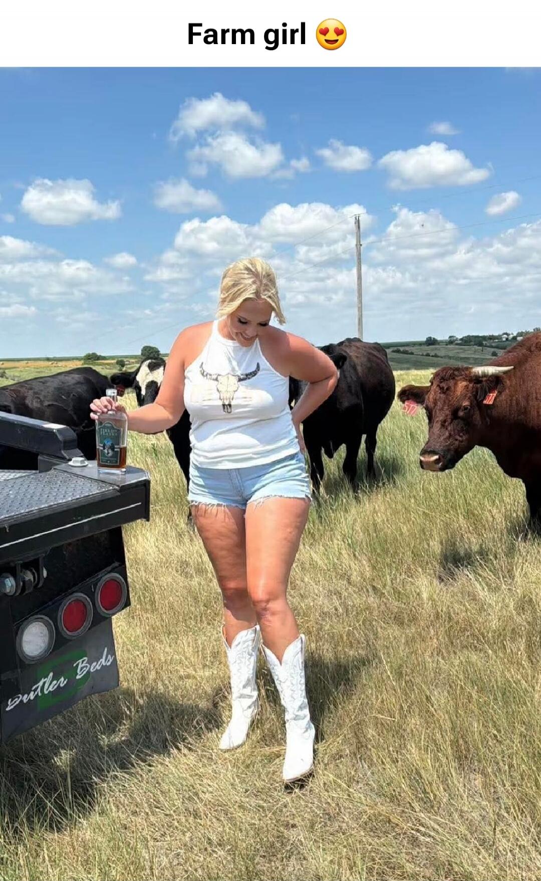 Farm girl 😍. Butler Beds. A woman is standing in a field with cows, holding a bottle of alcohol.