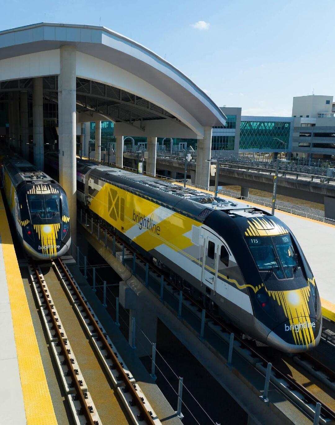 Two Brightline trains are parked at a modern station. The trains are black, yellow, and silver, with 'brightline' branding visible on their sides and front. One train has the number '115' displayed.