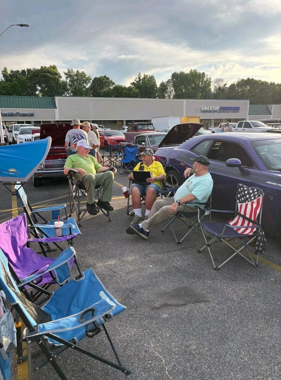 Franklin Financial, ONESTOP FURNITURE, FURNITURE-APPLIANCES-ELECTRONICS, SUN, JEEP. A group of men are gathered in a parking lot with classic cars, sitting in folding chairs.