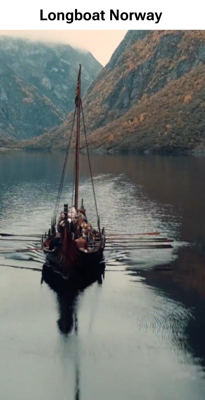 Longboat Norway. A longboat, resembling a Viking ship, with people on board, sails on a calm body of water, likely a fjord, surrounded by majestic mountains.