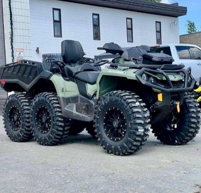 Two six-wheeled all-terrain vehicles (ATVs) parked side by side outside a building.