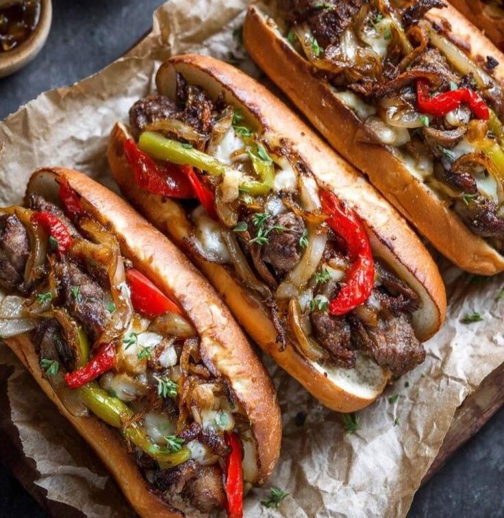 Three loaded beef sandwiches with sautéed peppers and onions on toasted buns.