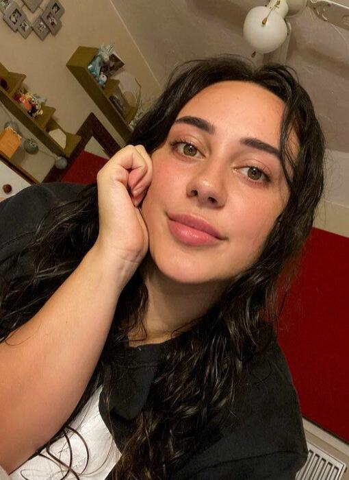 Portrait of a young woman with long dark hair resting her chin on her hand.