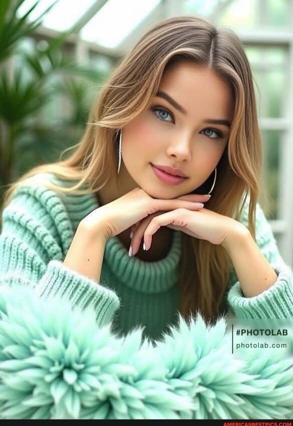 Portrait of a woman in a mint green sweater with long, light brown hair, resting her chin on her hands.