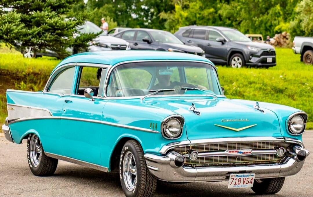 A classic turquoise 1957 Chevrolet Bel Air. The license plate reads 'Massachusetts 718 VS4 The Spirit of America'. The tires are 'Daytona SR'.