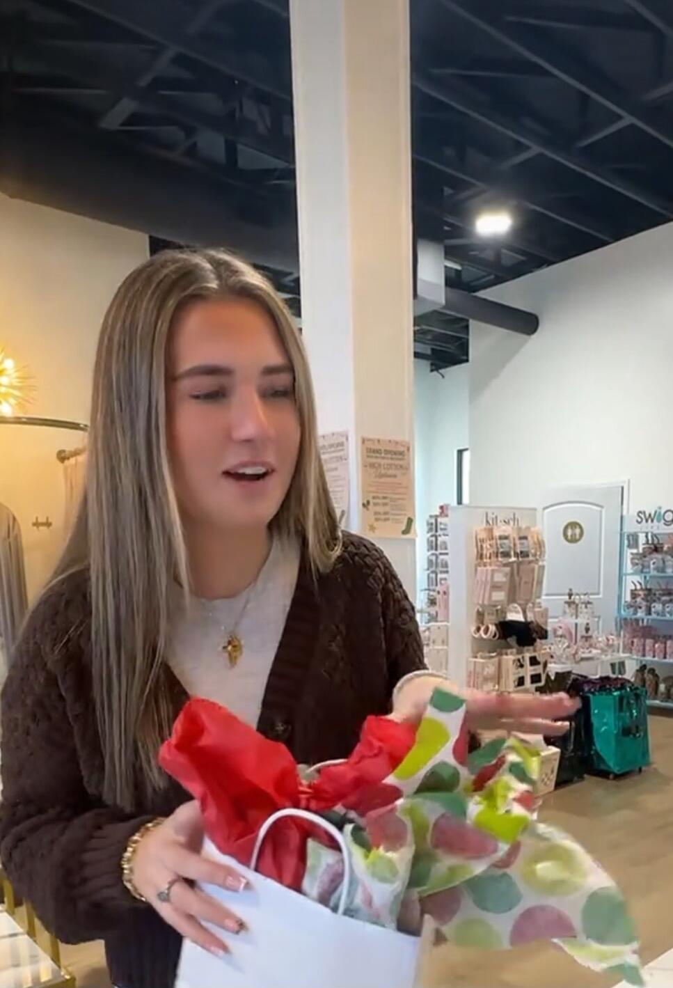 A woman in a shop holding a gift bag with colorful tissue paper.